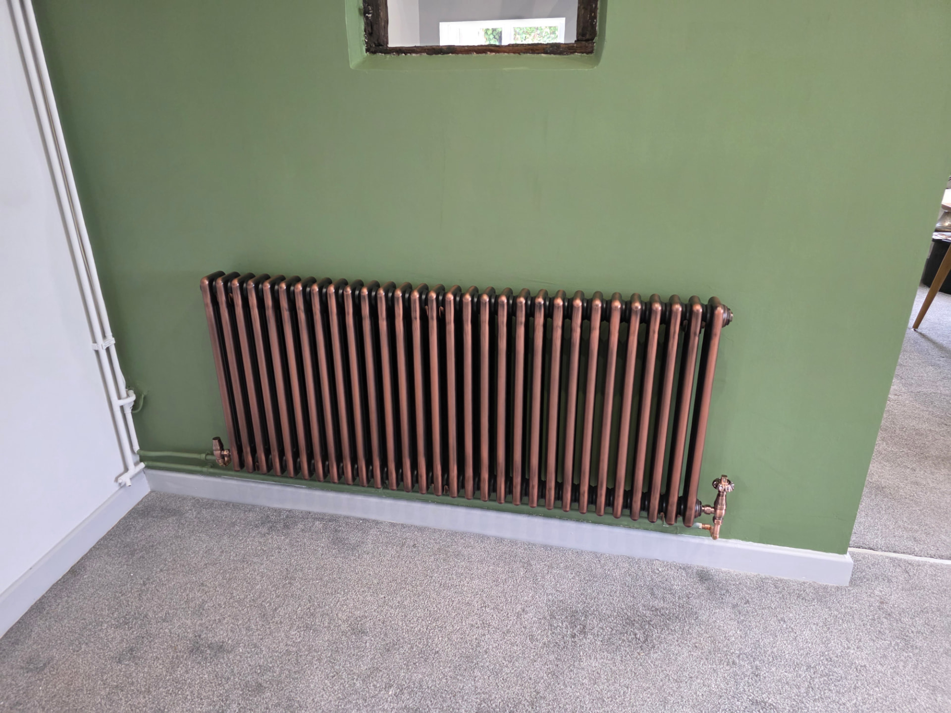 Wide copper-finish column radiator on a sage feature wall, traditional valves