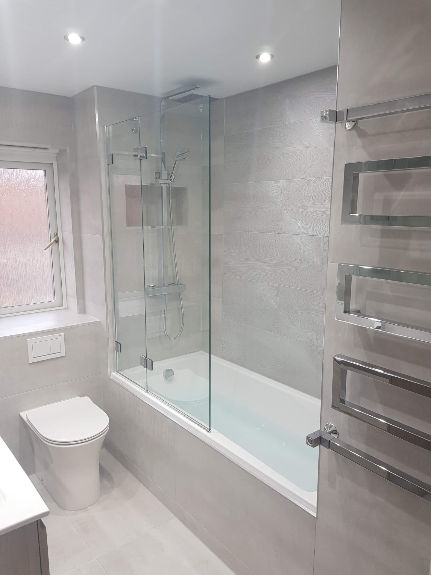 White & grey family bathroom with glass bath screen & designer chrome towel rail