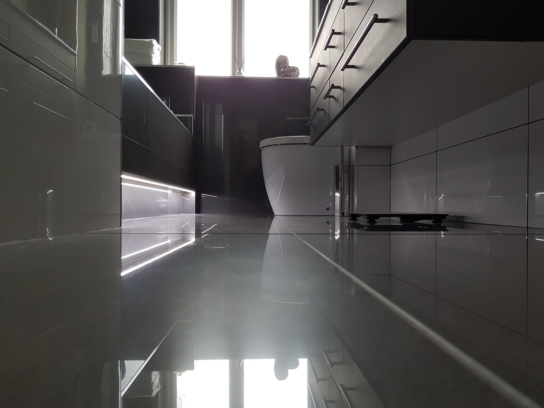 Low-angle detail of a modern black bathroom with LED plinth lighting & gloss cabinetry