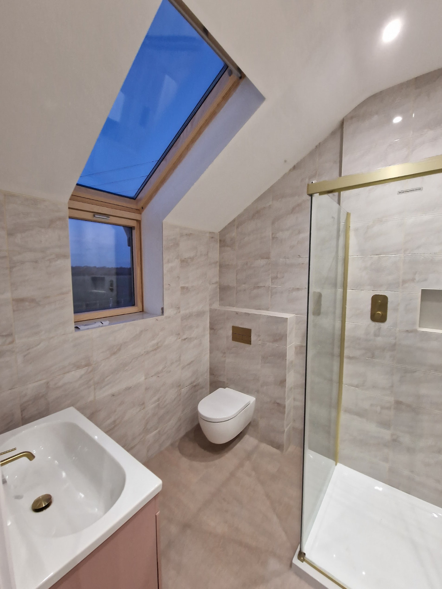 Loft shower room with gold-trim glass enclosure, wall-hung WC & skylight
